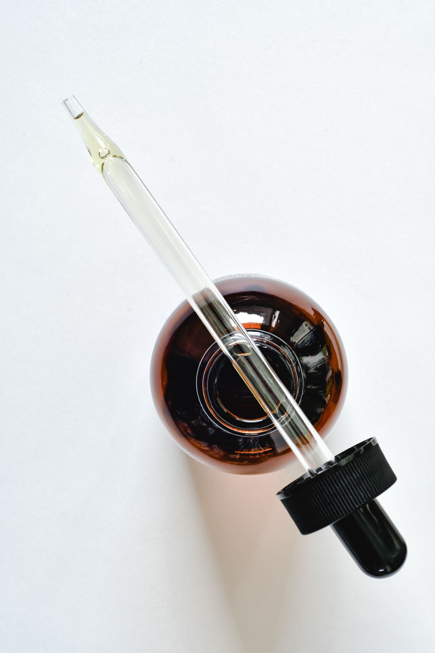 An amber glass bottle with a glass pipette on a light background