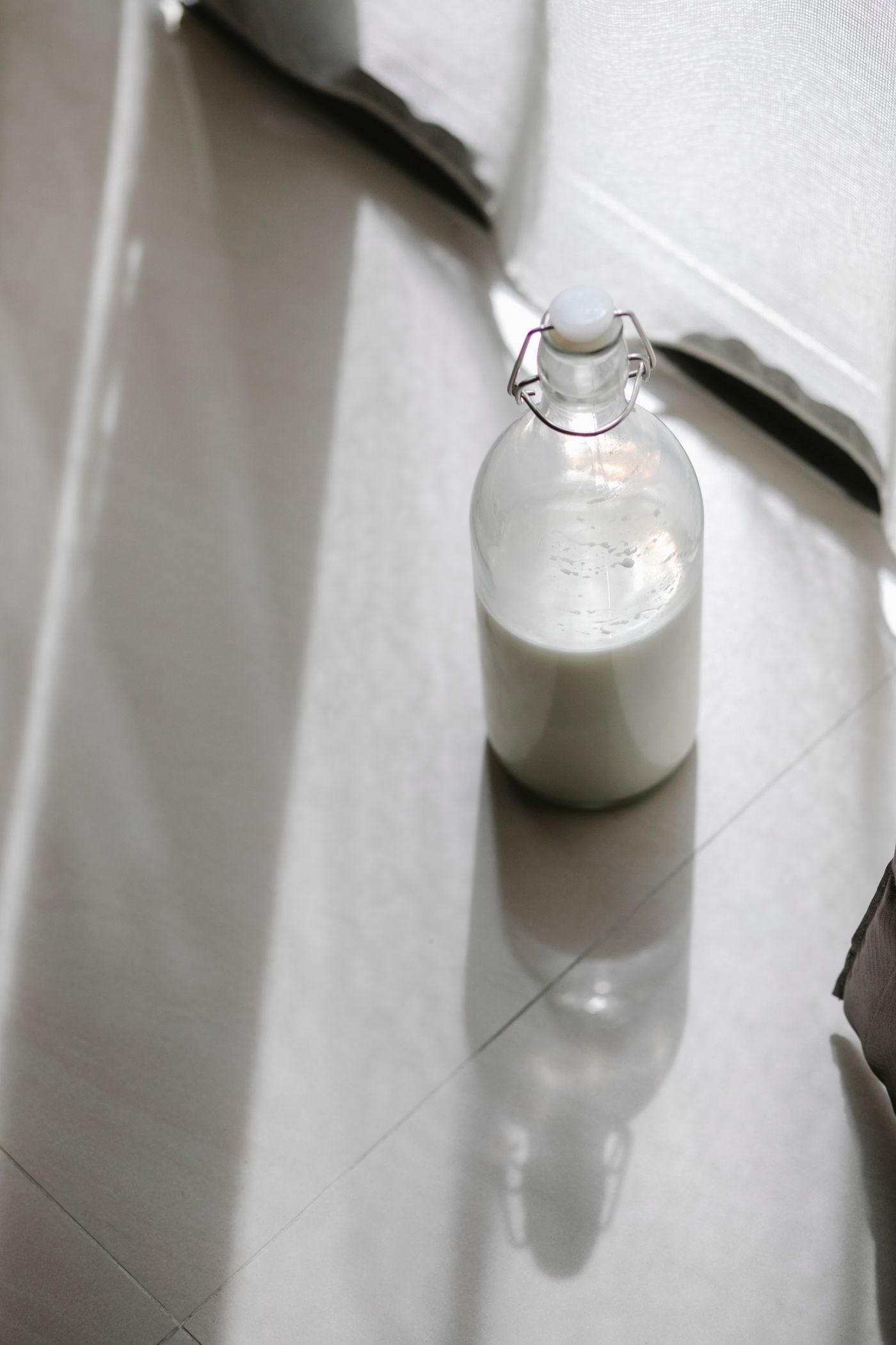 A clear swing-top glass bottle containing milk in soft window light