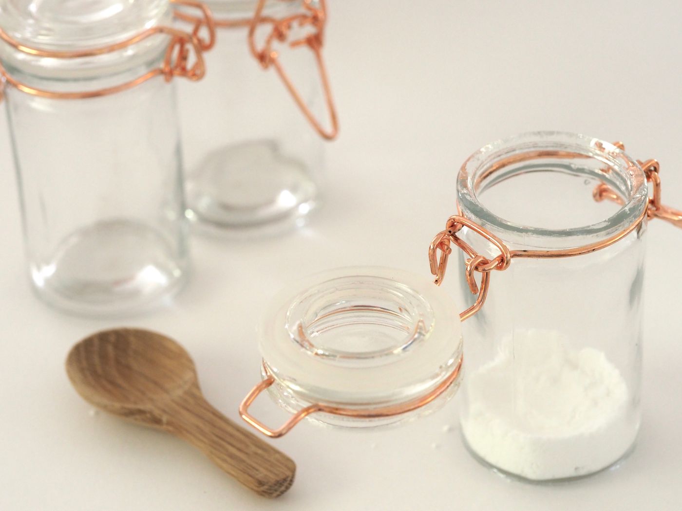Clear storage jars with copper-coloured clip closures and a wooden spoon on a light surface