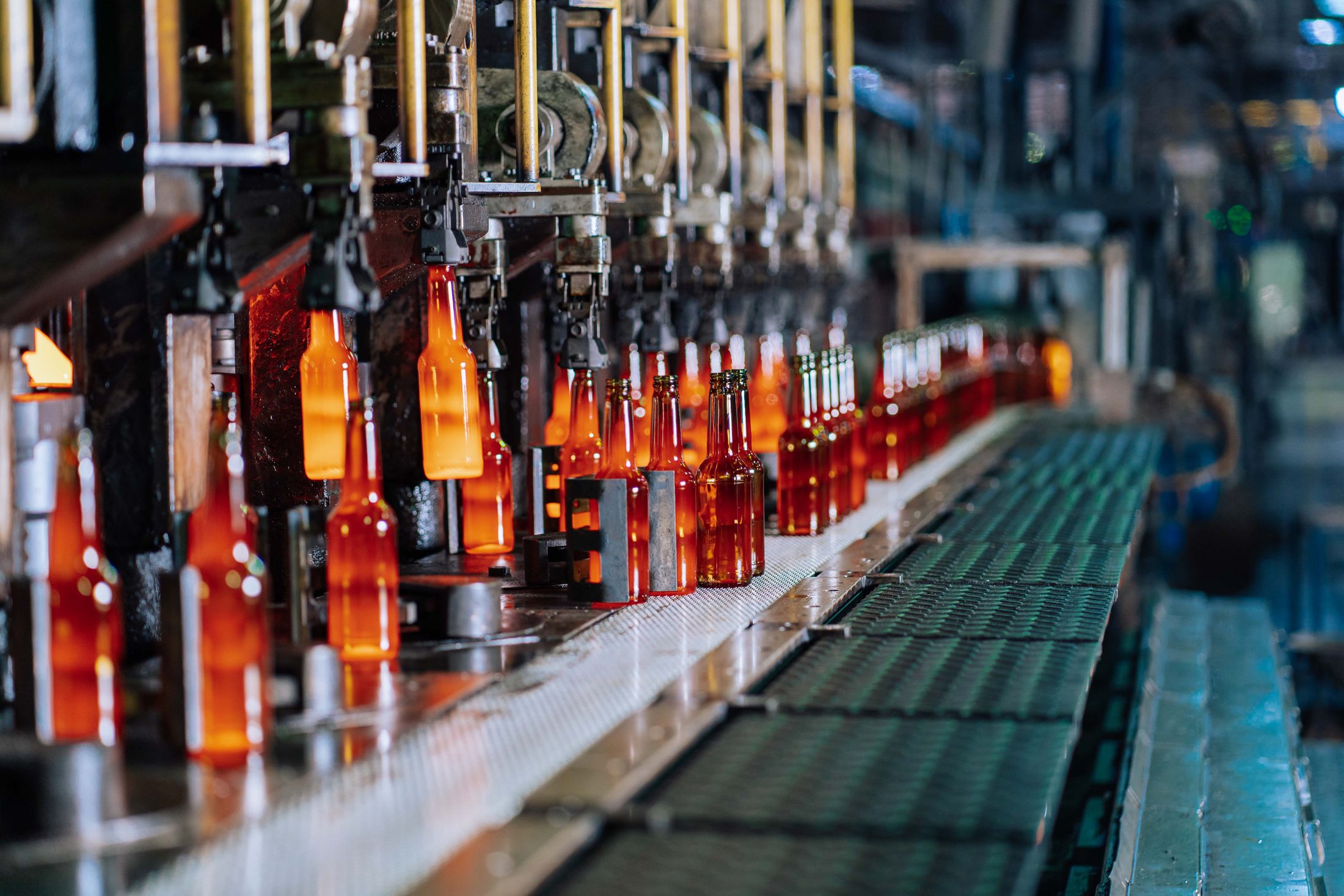 Glowing glass bottles being formed on an automated production line; industry stock photograph