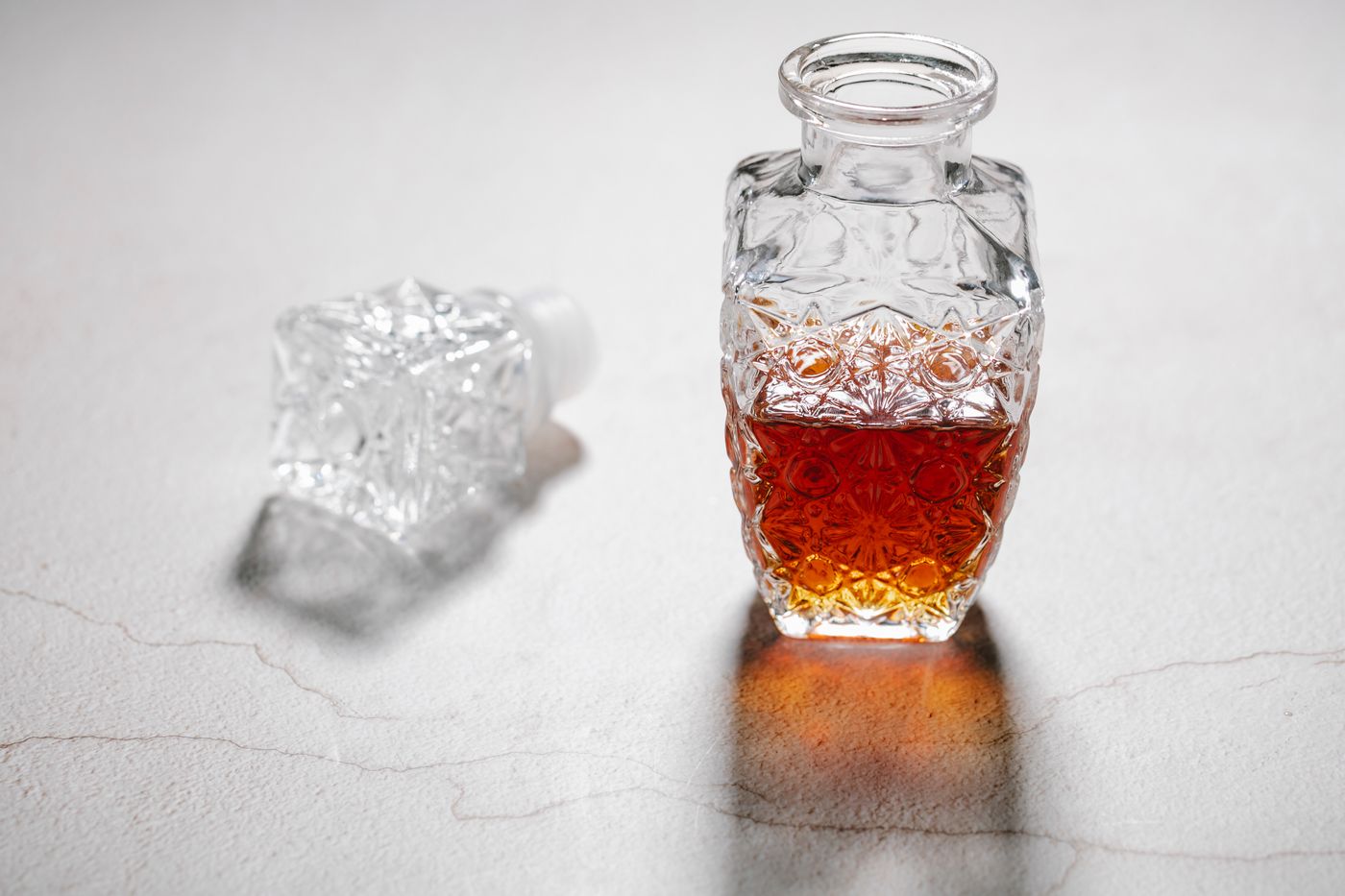An unlabelled patterned glass spirits decanter with amber liquid and a glass stopper