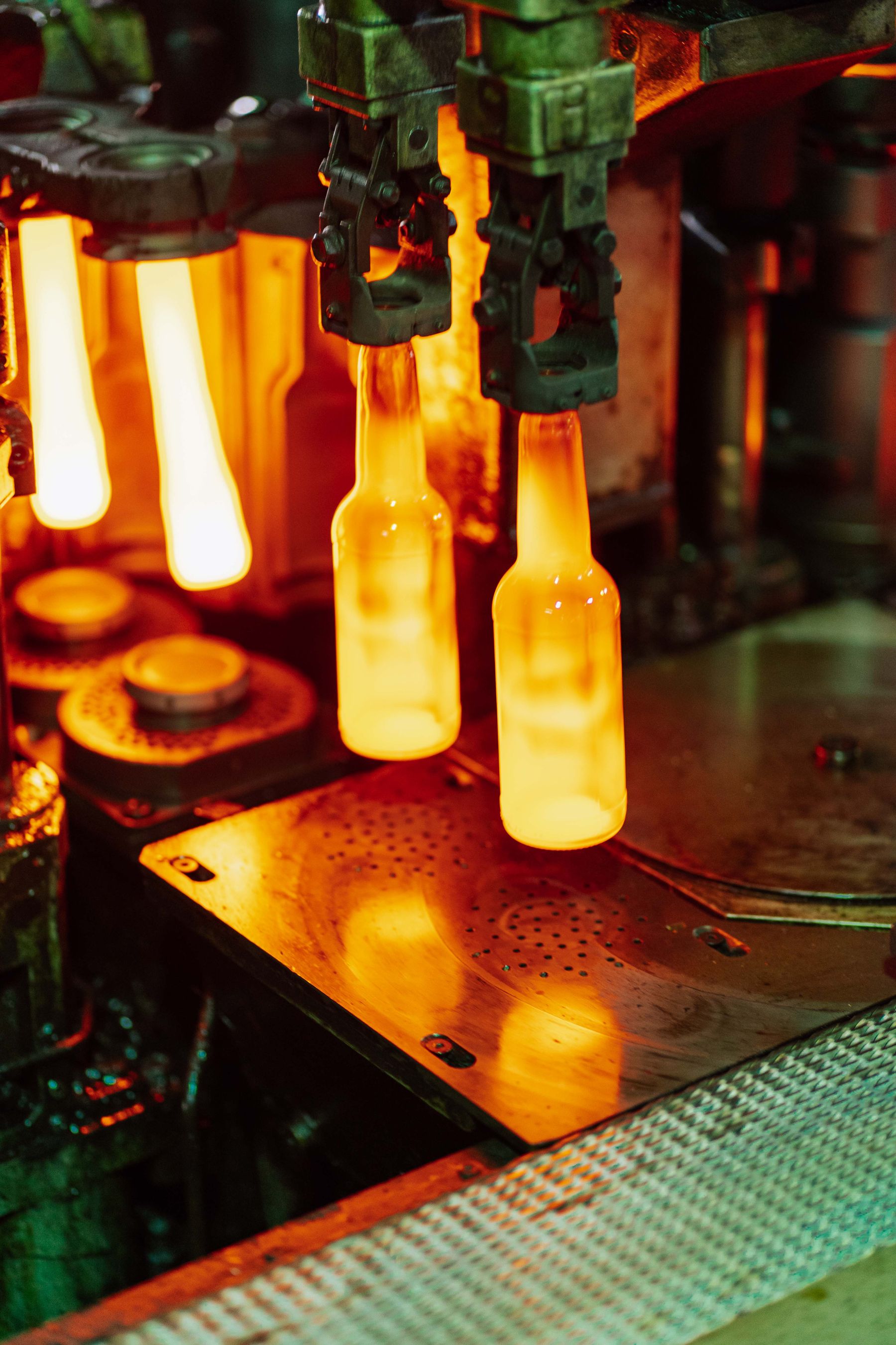 Glowing bottles held by automated glass-forming equipment; industry stock photograph